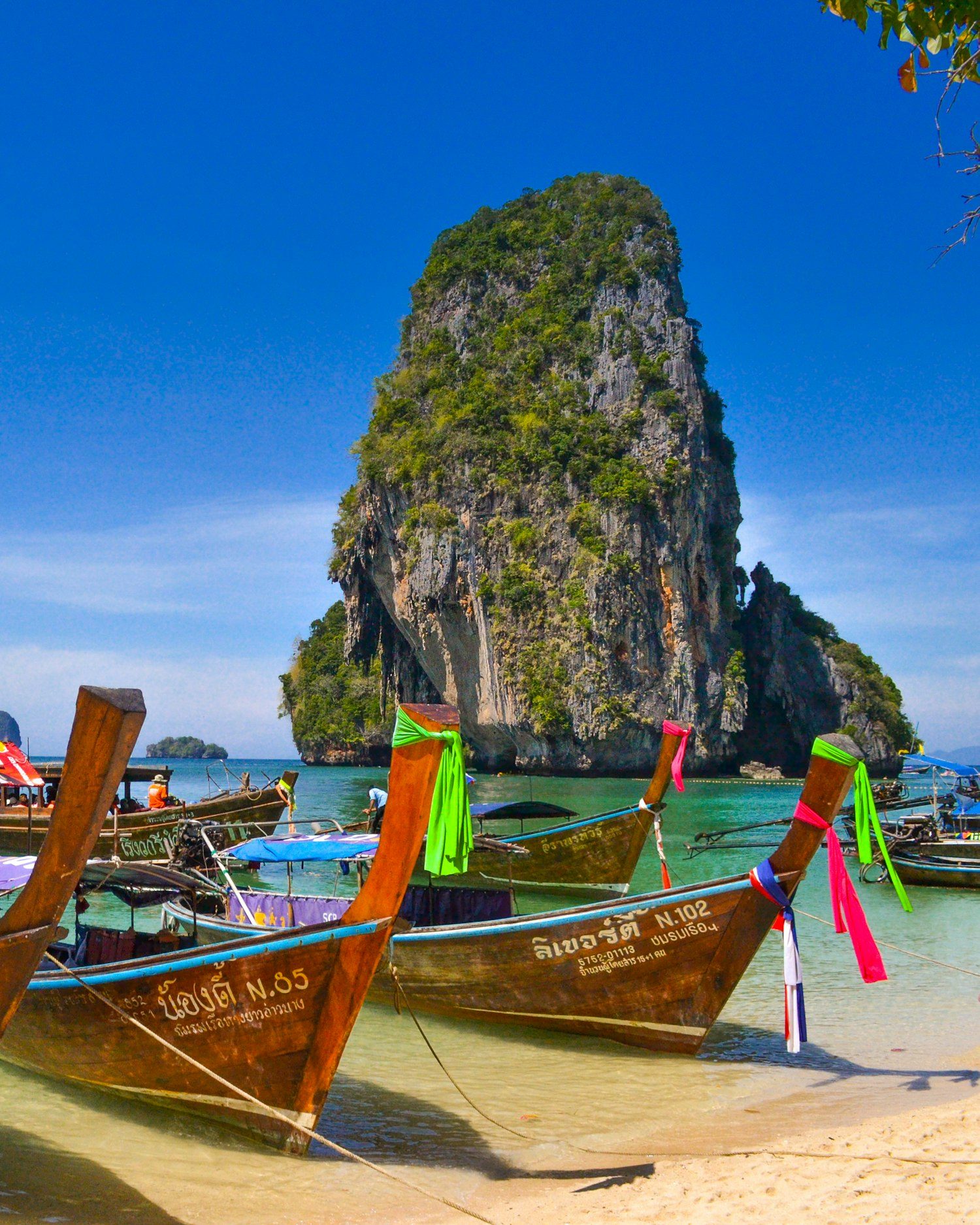 Bateaux traditionnels sur une eau turquoise au pied des falaises calcaires, en Thaïlande